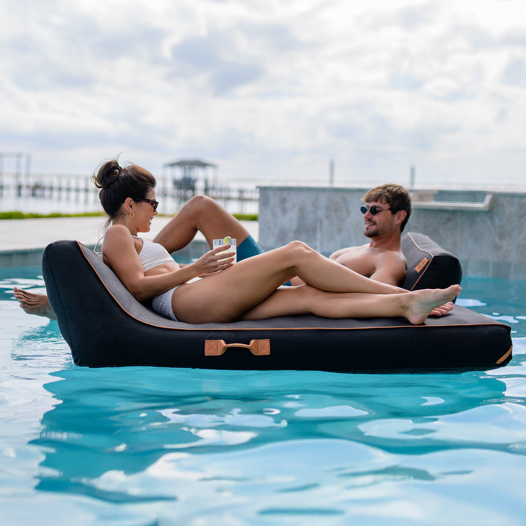 Two people relaxing on a inflatable pool float in a pool. #color_twilight-sunbrella-fabric