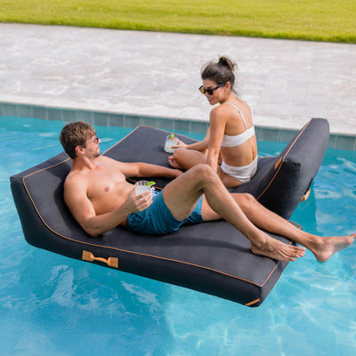 Two people relaxing on a floating inflatable lounge in a pool. 