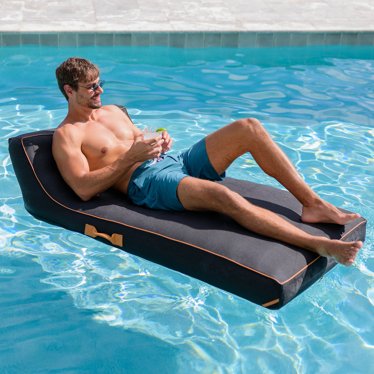 Man lounging on a black pool float in a pool 