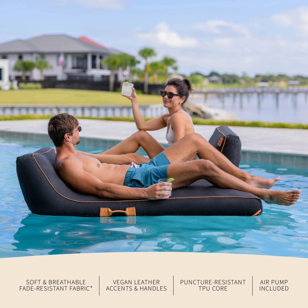 Two people relaxing on a floating inflatable lounger by a pool. #color_twilight-sunbrella-fabric