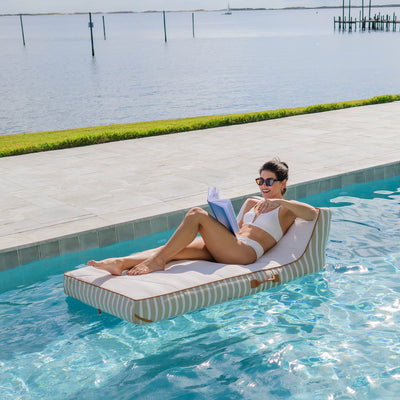 Woman relaxing on a striped pool float by a pool with water in the background 
