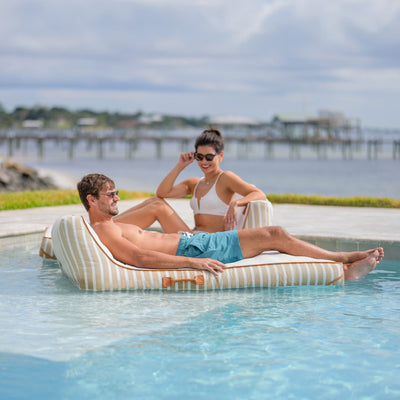 Man and woman relaxing on a striped inflatable lounger by a pool with a scenic background. 