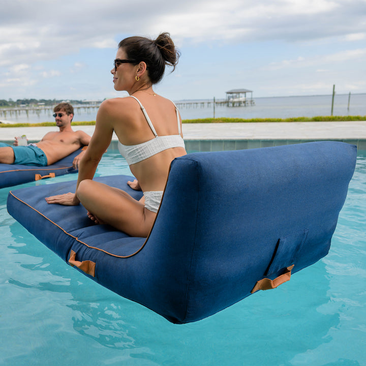 Two people relaxing on inflatable lounge chairs in a pool with a scenic background. #color_harbor-blue-sunbrella-fabric