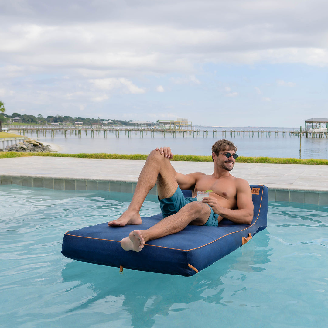 Man lounging on a blue inflatable pool float by a pool with a scenic background #color_harbor-blue-sunbrella-fabric