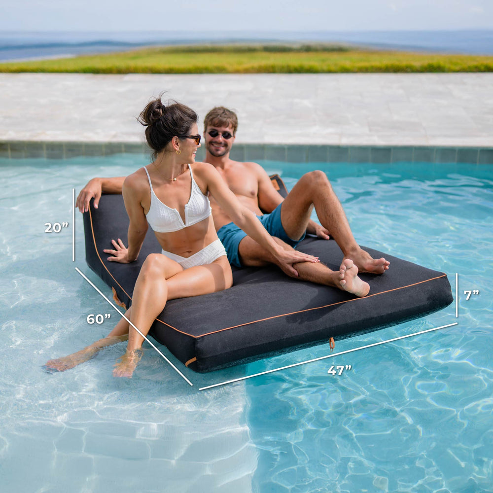 Two people sitting on a floating platform in a pool with dimensions displayed. #color_twilight-sunbrella-fabric