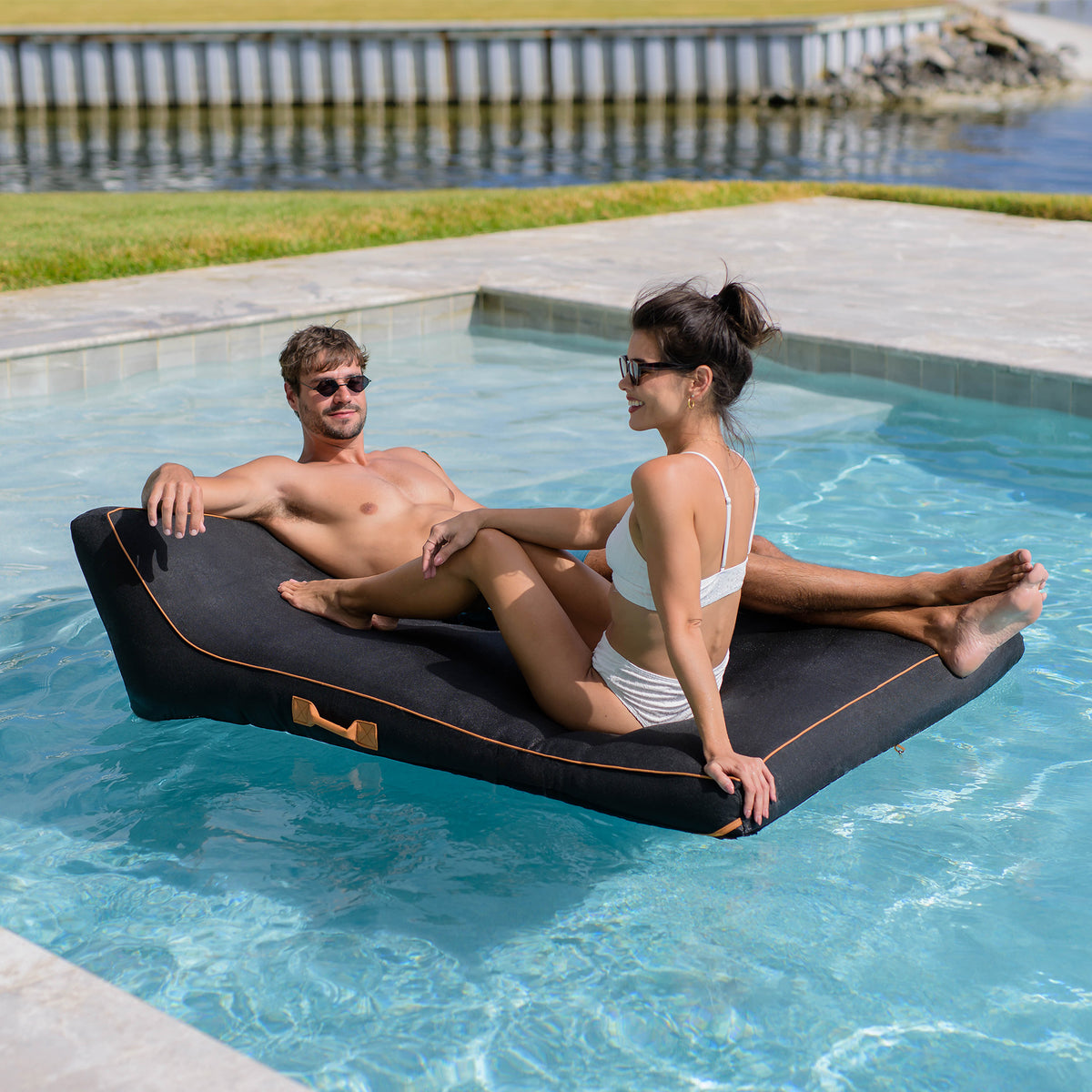 Two people relaxing on a floating platform in a pool. 