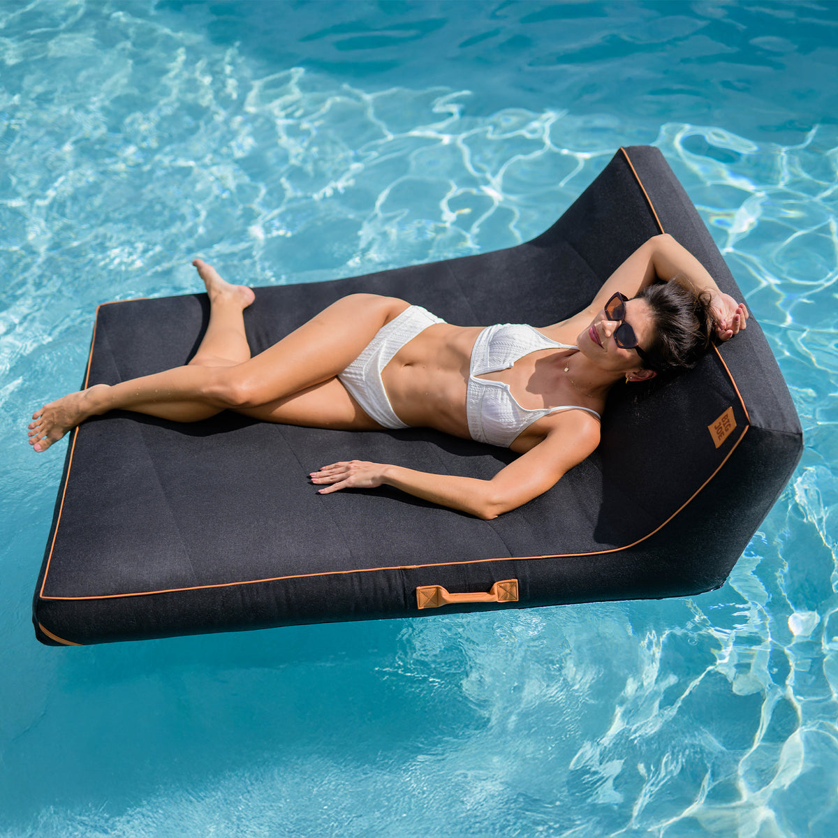 Woman lying on a black inflatable pool lounger in clear blue water 