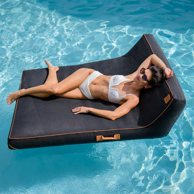 Woman lying on a black inflatable pool lounger in clear blue water 