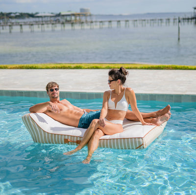 Two people relaxing on a pool float by a pool with a scenic background 