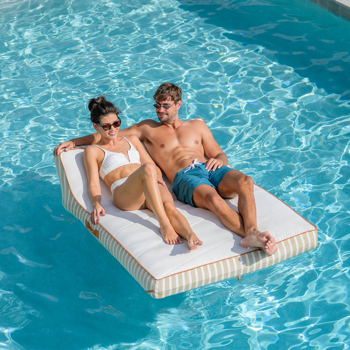 Two people relaxing on a floating platform in a pool #color_harbor-blue-sunbrella-fabric