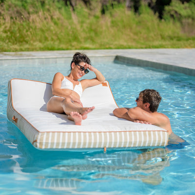 Two people relaxing on a striped pool float in a swimming pool. 