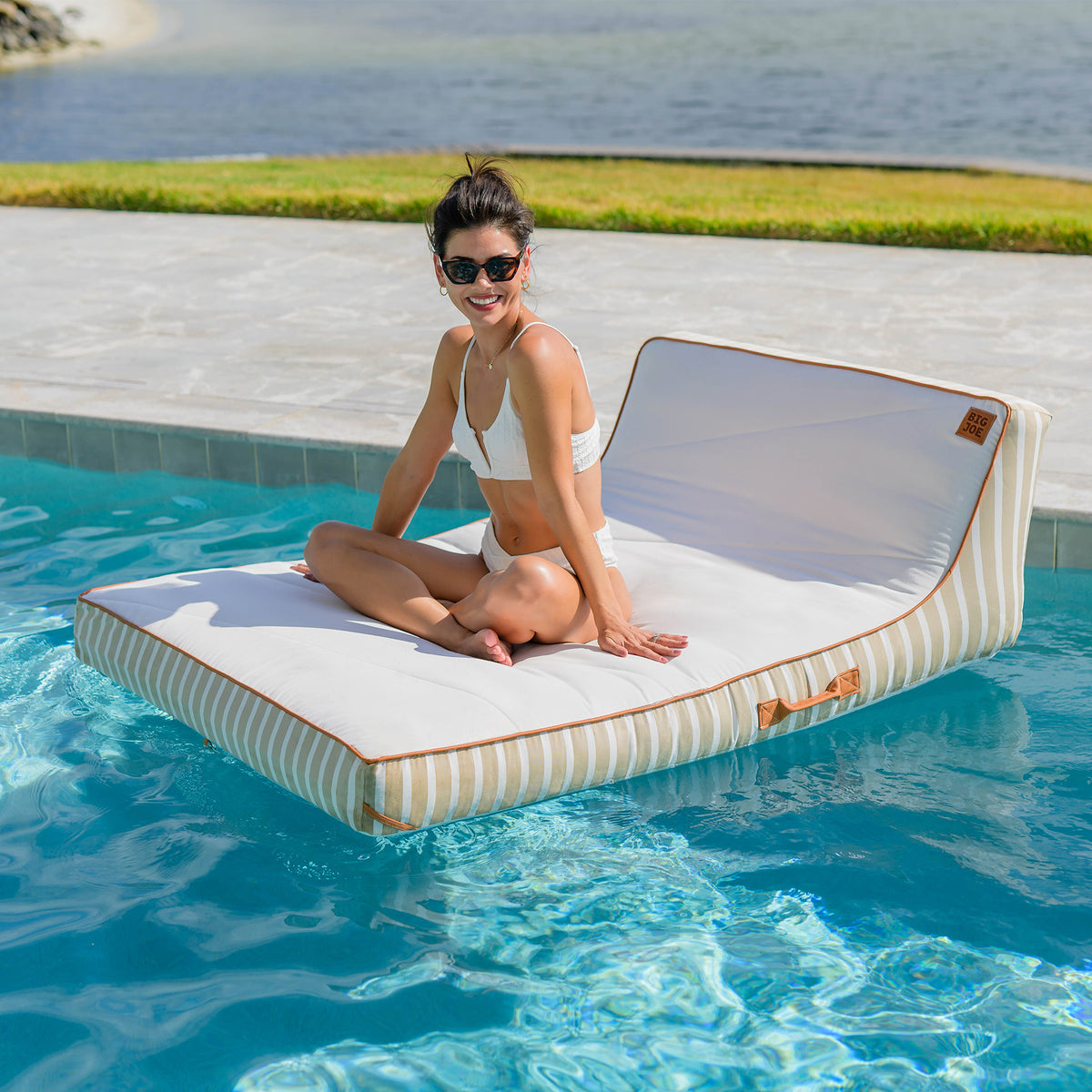 Woman sitting on a striped pool float in a pool with a scenic background 