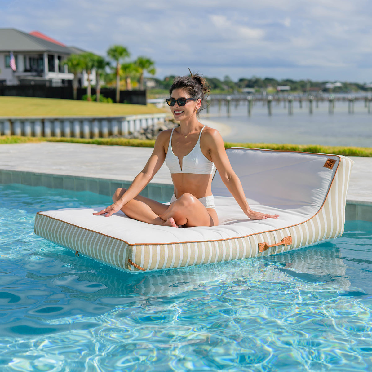 Woman sitting on a floating platform in a pool with a scenic background 