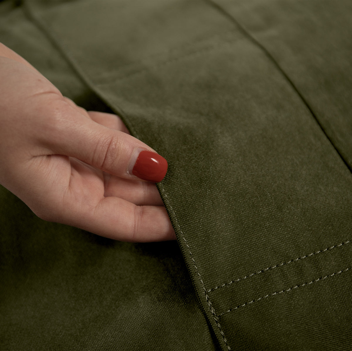 Close-up of a hand with red nail polish touching the edge of a green fabric 