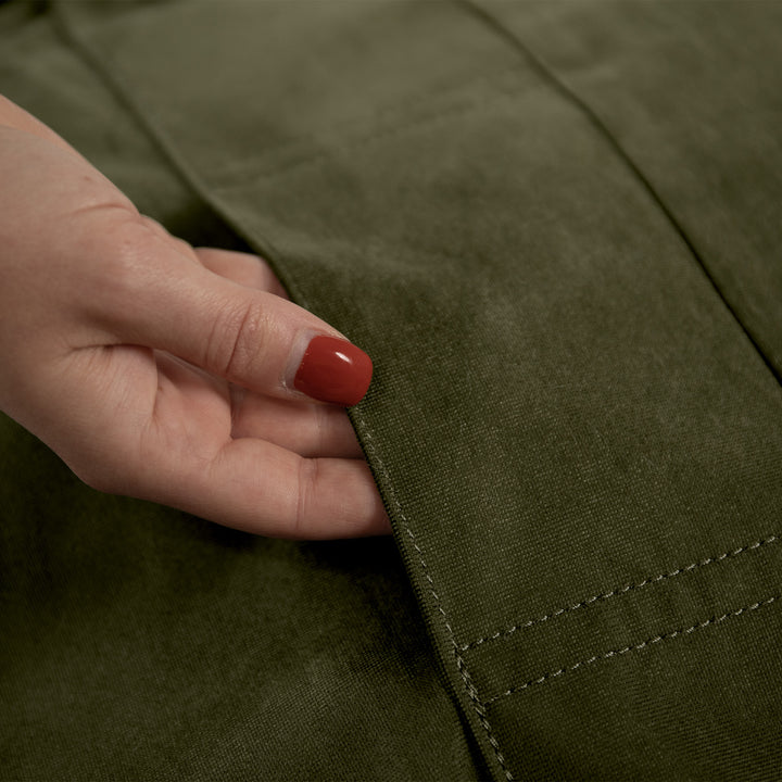 Close-up of a hand with red nail polish touching the edge of a green fabric #color_forest-green-velveteen
