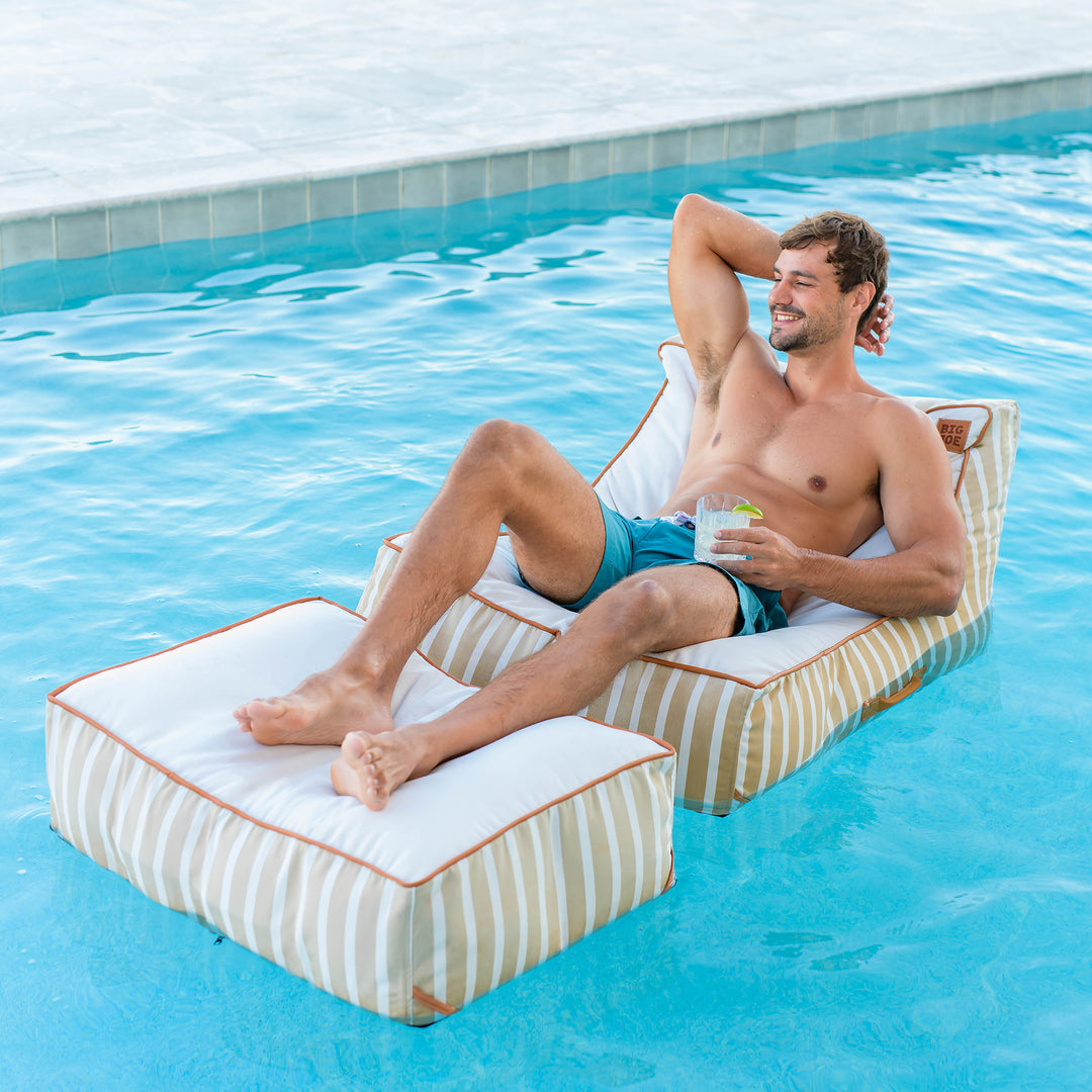 Man relaxing on a striped pool float in a swimming pool #color_sand-stripe-sunbrella-fabric