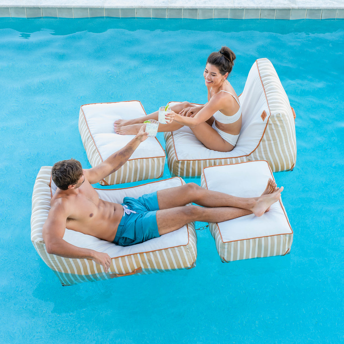 Two people relaxing on pool chairs in a pool. 