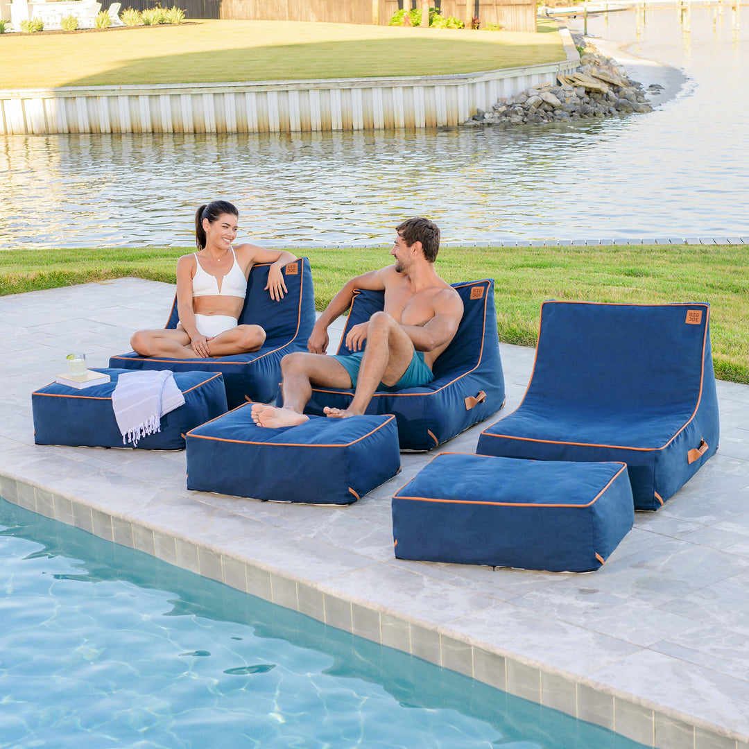 Two people sitting on blue lounge chairs by a poolside. #color_harbor-blue-sunbrella-fabric