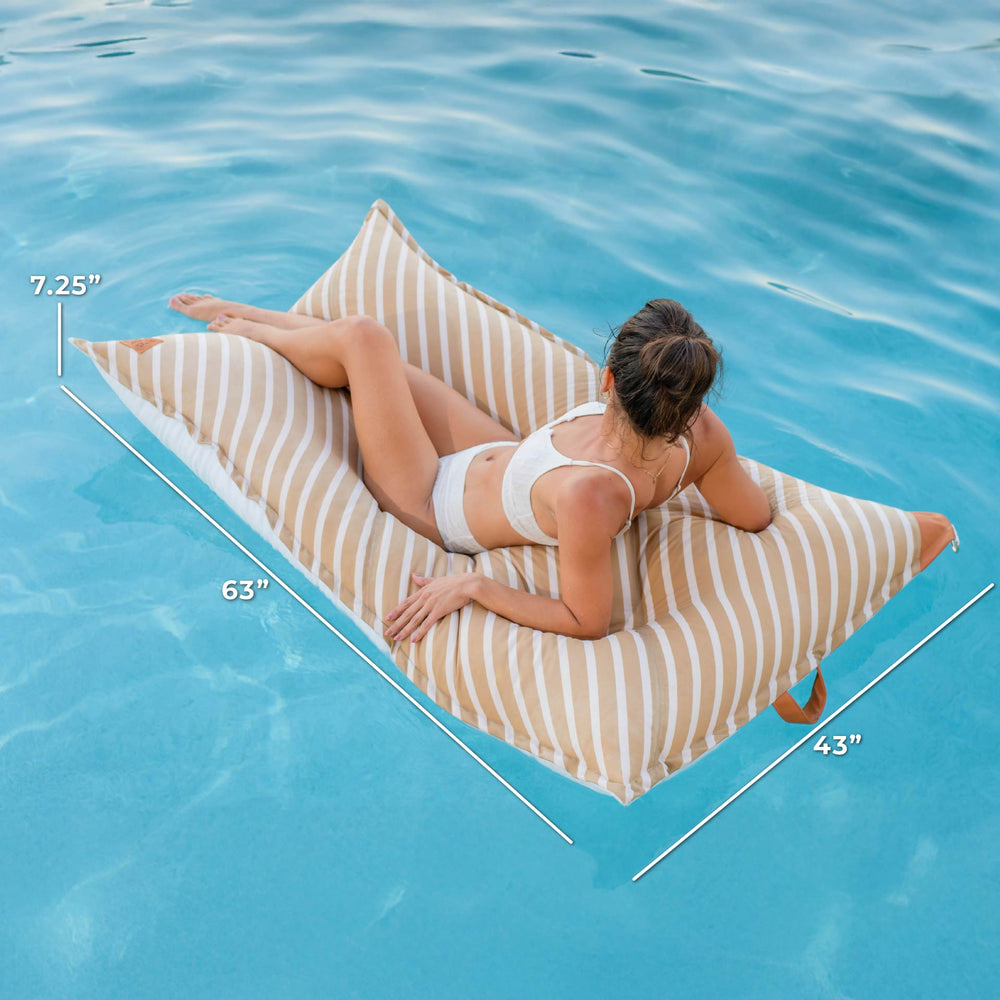 Woman lounging on a striped pool float with measurements overlaid, set against a blue pool background. #color_sand-stripe-sunbrella-fabric
