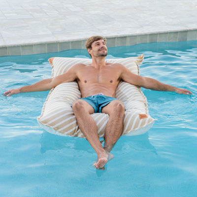 Man relaxing on a striped inflatable pool float in a pool. 