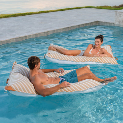 Two people relaxing on striped bean bags in a pool. 