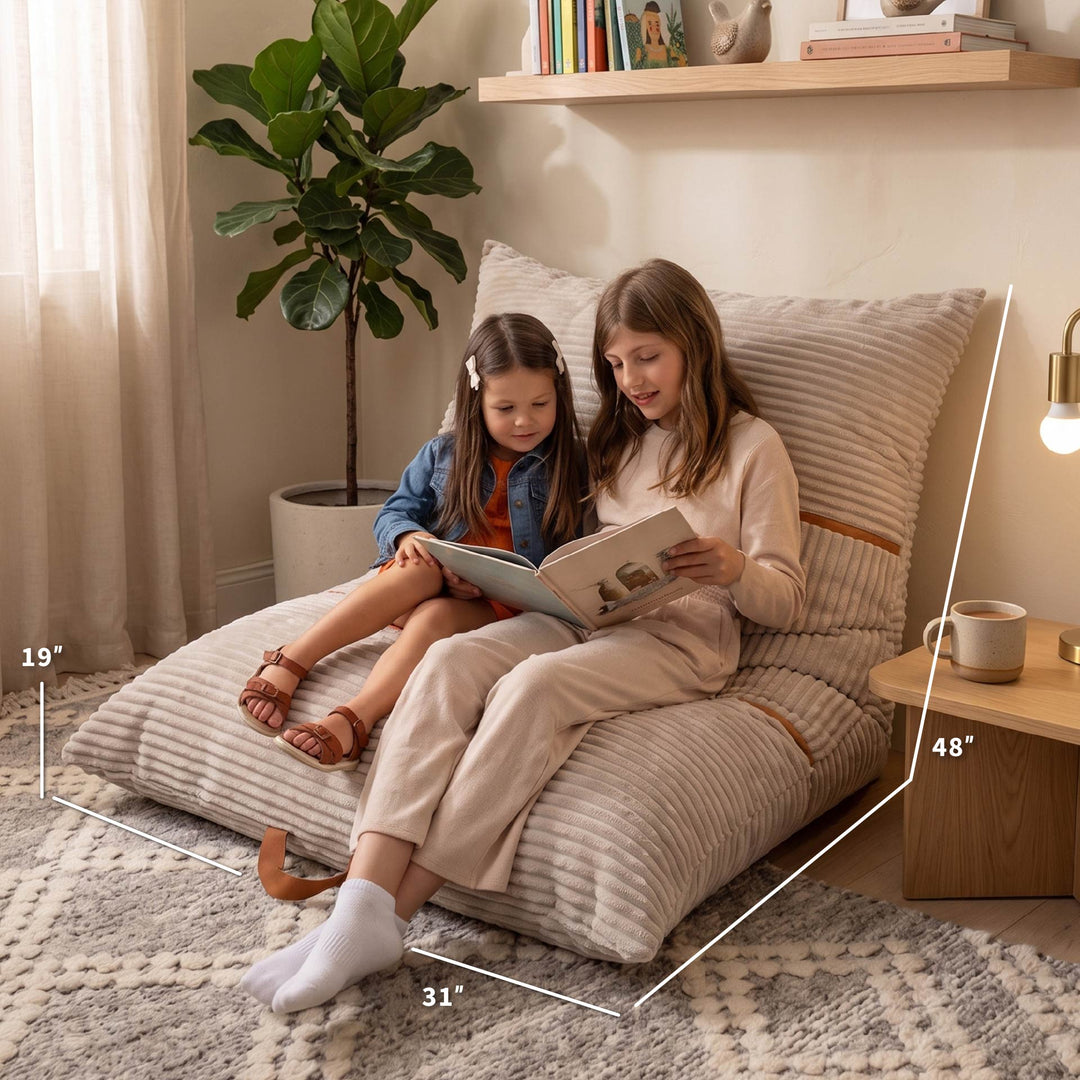 Two people sitting on a large striped beige lounge floor cushion in a cozy room, with white dimension lines showing the cushion&