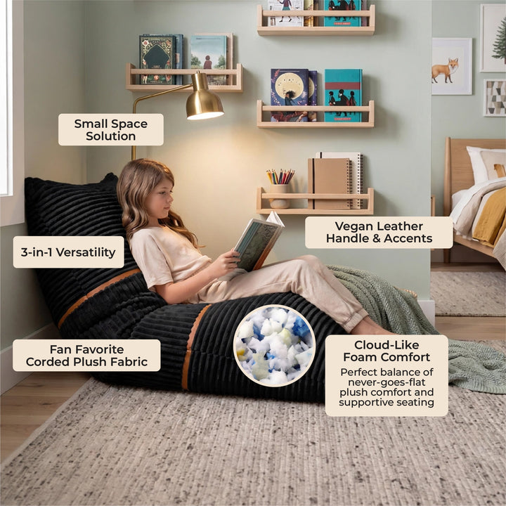 A child sits on a large black corded plush bean bag chair in a styled bedroom setting, with text callouts highlighting features like small space solution, 3-in-1 versatility, vegan leather handle and accents, fan favorite corded plush fabric, and cloud-like foam comfort. 