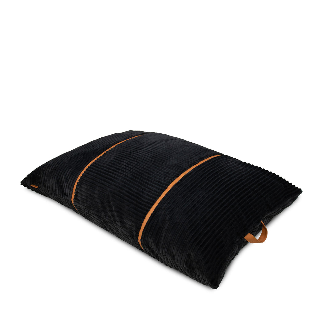 A black corduroy pillow with contrasting tan leather handles on two ends, shown on a clean white background. 