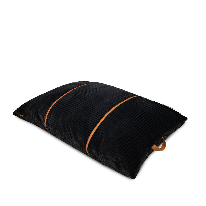 A black corduroy pillow with contrasting tan leather handles on two ends, shown on a clean white background. 