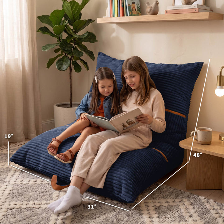 A large navy blue floor cushion set with two matching pillows in a styled room, with a woman and a child sitting on the cushion reading. White dimension lines and text overlays show the measurements: 48 inches tall, 31 inches wide, and 19 inches deep. 