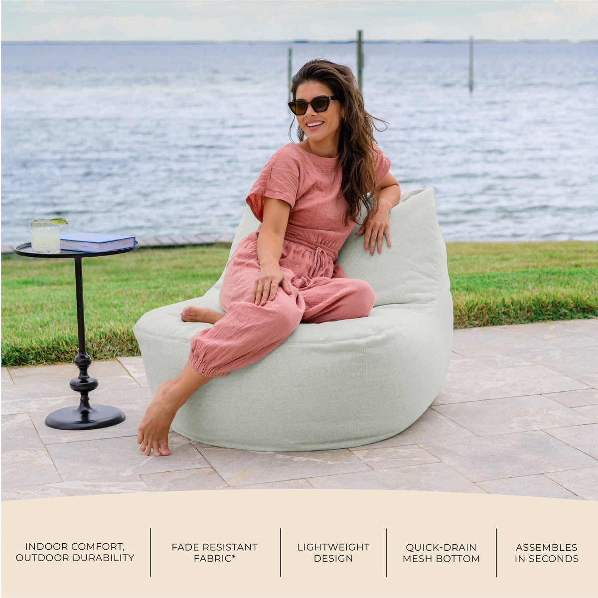 Woman sitting on a bean bag chair by the water with text about product features. #color_sunday-gray-outdoor-performance-linen