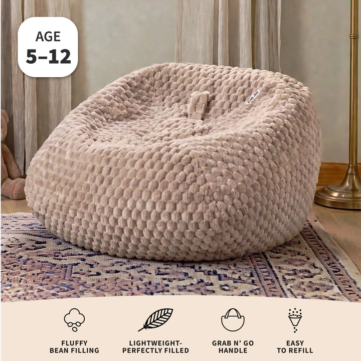 A large, round, textured beige bean bag chair sitting on a patterned rug in a living room setting. The image includes an &