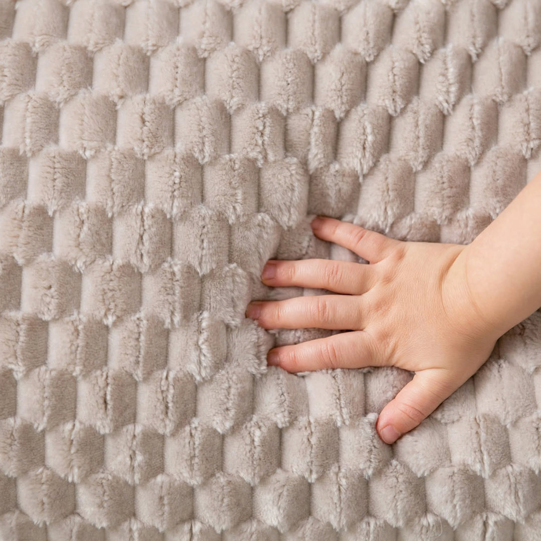 A close-up of a textured, plush fabric surface in a warm taupe-beige color, with a child&