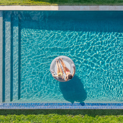 Person floating on a pool float in a swimming pool with green grass surrounding it 