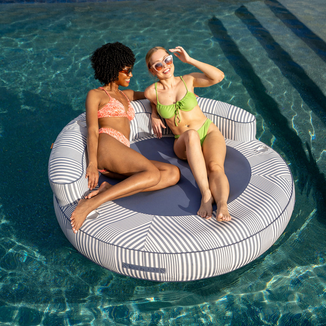 Two women sitting on a striped pool float in a pool #color_weekend-navy-stripe-olefin
