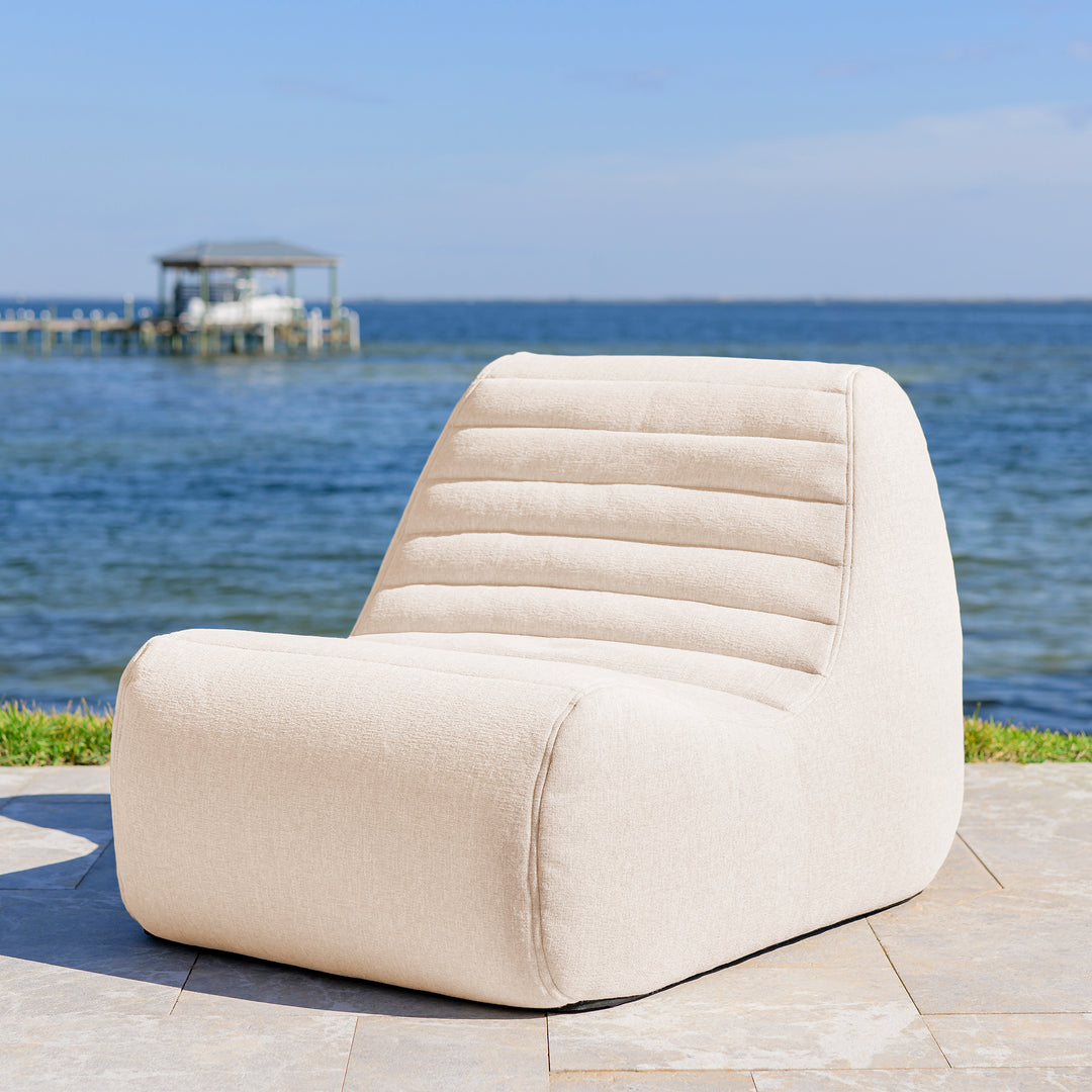 Beige chair by a body of water with a dock in the background #color_sunlit-cream-outdoor-performance-linen
