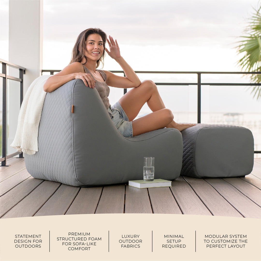 Woman relaxing on a modern outdoor sofa with a view of a balcony and ocean. #color_moonlit-gray-outdoor-vegan-leather