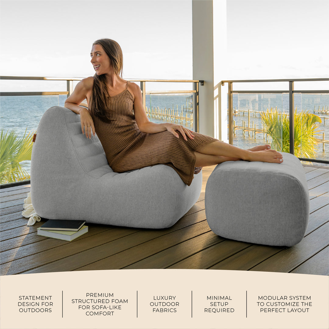 Woman sitting on a modern outdoor chair with a scenic background #color_port-gray-outdoor-performance-linen