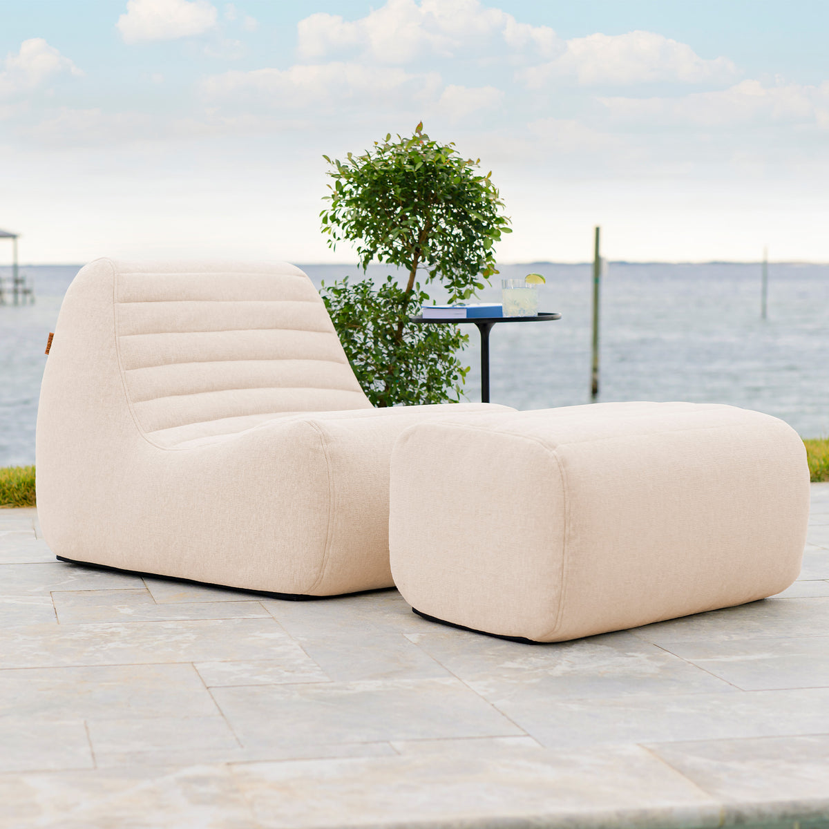 Beige outdoor lounge chair and ottoman on a patio with a scenic background. 