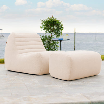 Beige outdoor lounge chair and ottoman on a patio with a scenic background. 