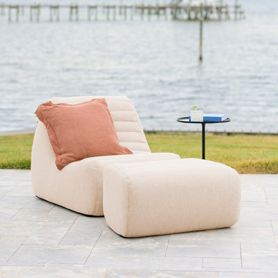 Beige outdoor chair with a pink pillow on a patio near a body of water. 