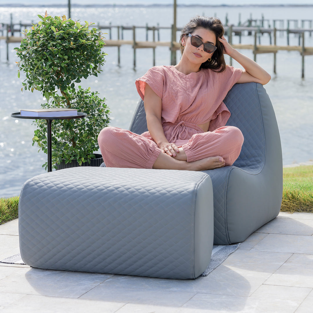 Woman sitting on a modern outdoor chair by a waterfront #color_moonlit-gray-outdoor-vegan-leather