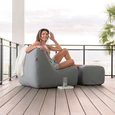 Woman sitting on a modern gray lounge chair on a wooden deck. 