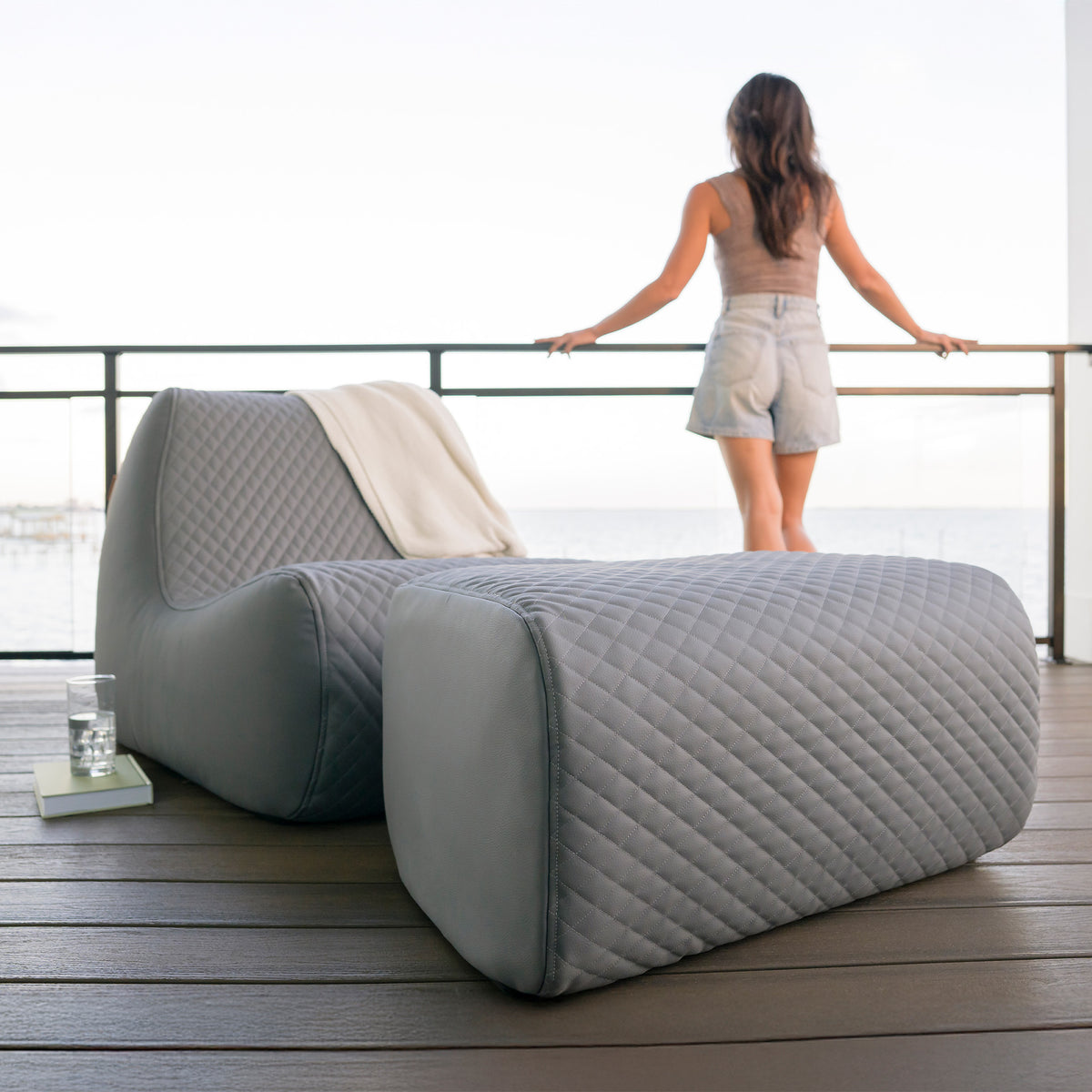 Modern outdoor furniture set on a wooden deck with a woman standing in the background. 