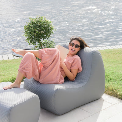 Woman relaxing on a gray outdoor bean bag chair by a body of water. 