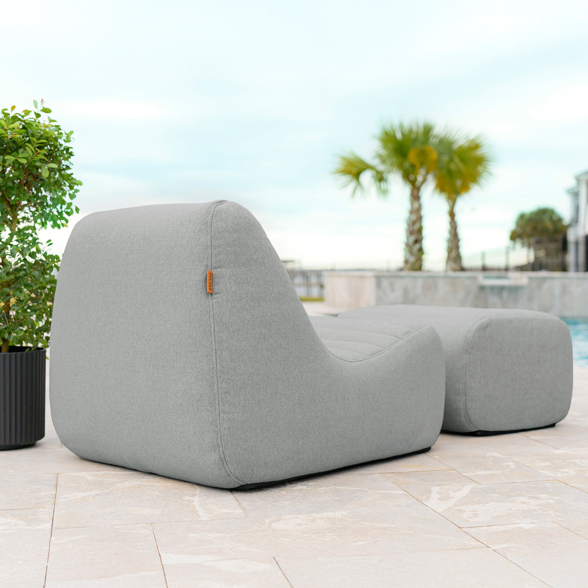 Gray outdoor lounge chair on a patio with pool and palm trees in the background 