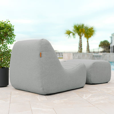 Gray outdoor lounge chair on a patio with pool and palm trees in the background 