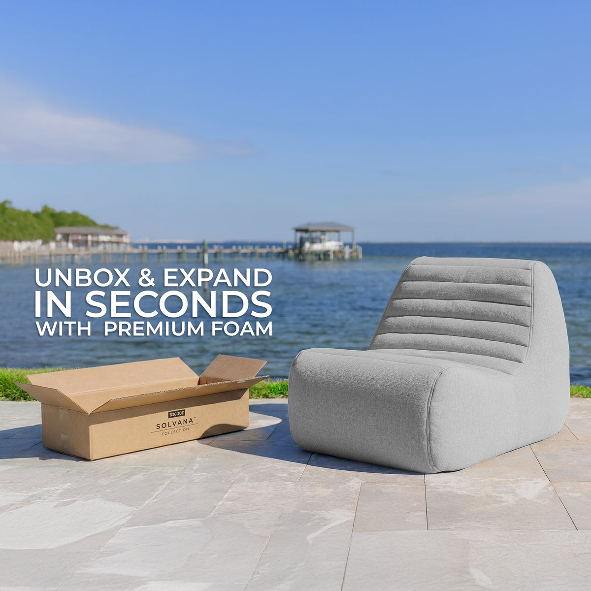 Gray outdoor chair next to a cardboard box with text 'Unbox & Expand in Seconds with Premium Foam' by Solvana, set against a scenic waterfront background. 