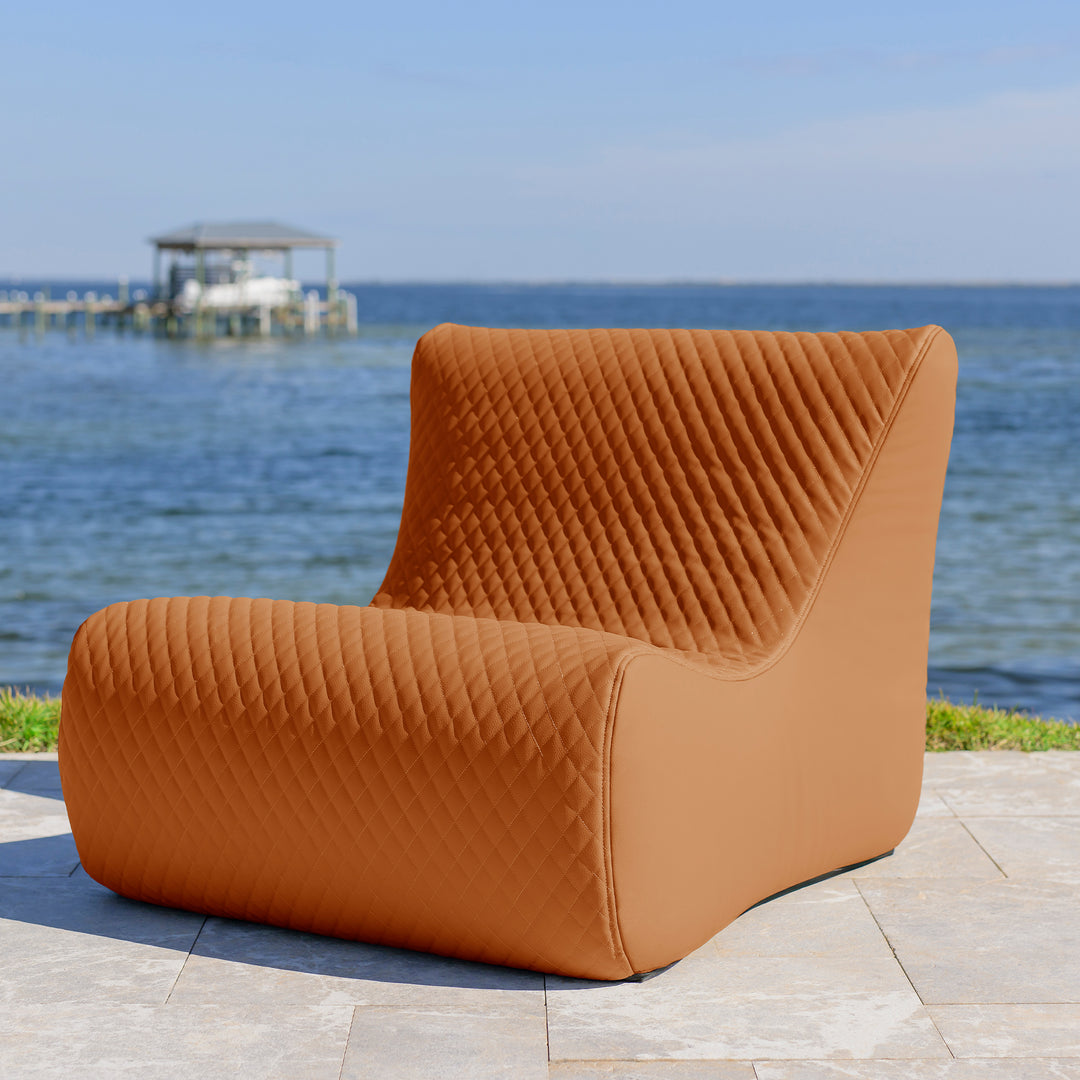 Brown quilted chair on a patio with a scenic ocean view #color_honey-sand-outdoor-vegan-leather