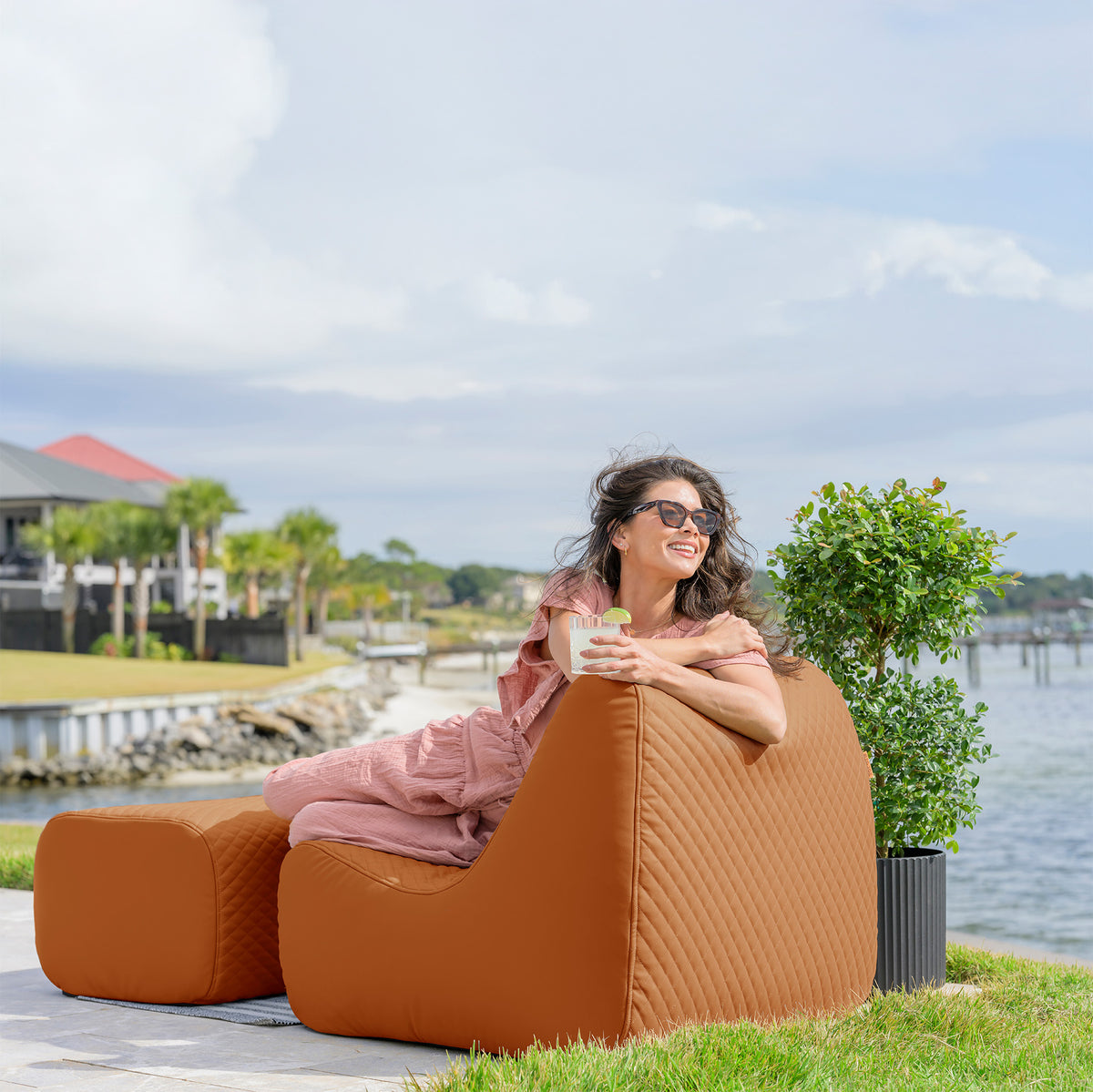 Woman sitting on a brown outdoor chair by a waterfront with a scenic background 